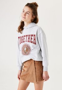Heather-grijze hoodie met de voorprint "TOGETHER" in het rood, gecombineerd met een tan corduroy rok met verticale strepen en een zijsplit.