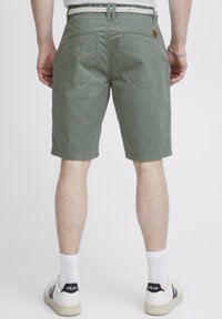 Pantalones cortos de algodón verde con un ajuste relajado, que cuentan con bolsillos traseros y un cinturón tejido. Combinados con calcetines blancos y zapatillas blancas.