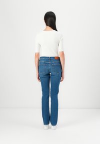 Skinny blue jeans with a mid-rise waist, featuring a brown leather patch on the back, back pockets, and a denim texture.