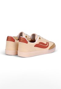 Beige sneakers with brown suede accents and red logo. Features a low-top design, round toe, and textured side panels. Soft, rubber sole.