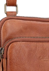 Borsa a spalla in pelle marrone con superficie testurizzata, zip in metallo e una tracolla robusta con gancio in metallo. Marchio evidente impresso.