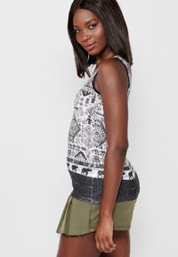 Čierny a biely tank top s geometrickým vzorom, skombinovaný so zelenou, skladanou mini sukňou. Látka vyzerá mäkko a štruktúrovane.