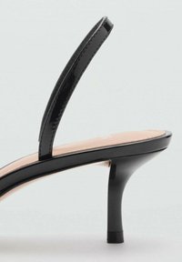 Sandale cu toc din piele patent neagră, cu o curea subțire și vârf întunecat. Prezintă un toc stiletto și un interior bej.