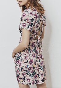Vestido corto floral con mangas cortas, presenta un fondo negro, flores rosa y crema, y un diseño de espalda descubierta con lazos.