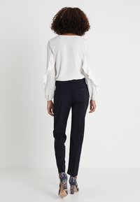 Vit blus med volangärmar, kombinerad med marinblå skräddarsydda byxor och högklackade skor med blommönster. Slät tyg, figurnära siluett.