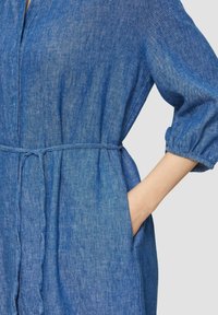 Blaues Jeanskleid mit lockerer Passform, drei Viertelärmel, tailliertem Schnitt und seitlichen Taschen. Leichter, strukturierter Stoff.