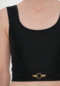 Top corto nero realizzato in un tessuto liscio, dotato di spalline larghe con il logo "JUST" in rilievo e un anello dorato decorato con dettagli ornamentali.