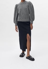 Szary wełniany sweter z bufkowymi rękawami, zestawiony z czarną spódnicą do kolan z bocznym rozcięciem. Czarne wsuwane buty dopełniają strój.