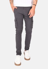 Pantaloni cargo grigi con due tasche laterali, design slim fit, realizzati in tessuto leggero, abbinati a sneakers bianche e a un top bianco con texture.