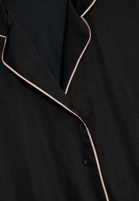 Svart pyjamaströja med kontrasterande ljusrosa kant längs kragen och knapplist, med en mjuk och smidig textur.