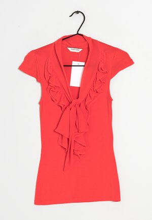 Czerwony dopasowany top z krótkimi rękawami, z falbanką z przodu i kokardą. Wykonany z miękkiego, elastycznego materiału o gładkiej teksturze.