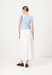 Haut bleu clair à côtes avec des manches volantes, associé à une longue jupe blanche brodée et des chaussures à talons marron.