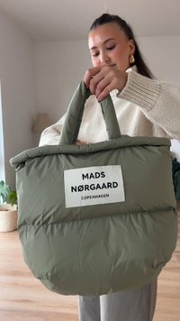 Saco tote acolchoado verde com alças robustas, apresentando um rótulo branco que diz "MADS NØRGAARD COPENHAGEN." Tecido suave e texturizado.