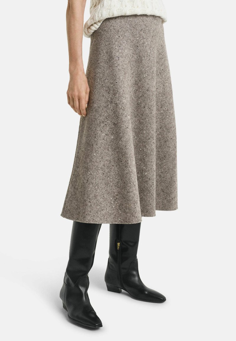 Jupe midi en laine grise avec une silhouette évasée, associée à des bottes en cuir noir hautes avec des zips sur les côtés et des pointes effilées.