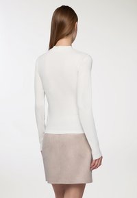 Top bianco a maniche lunghe con un design aderente, texture liscia e scollo tondo; abbinato a una gonna in suede grigia chiara.