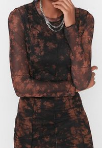 Top a maniche lunghe in rete nera con motivo tie-dye marrone. Presenta cuciture visibili e scollatura rotonda, abbinato a una collana doppia in argento con più catene.