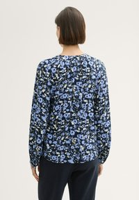 Niebieska bluzka w kwiatowy wzór z długimi rękawami, okrągłym dekoltem i plisowanymi detalami z tyłu. Lekki materiał o miękkiej fakturze.