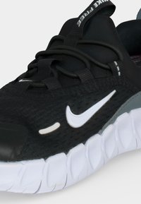 Μαύρο και γκρι αθλητικό παπούτσι Nike με λευκή σόλα, ευέλικτο σχέδιο, μαύρα κορδόνια και λευκό λογότυπο Nike swoosh στην πλευρά.