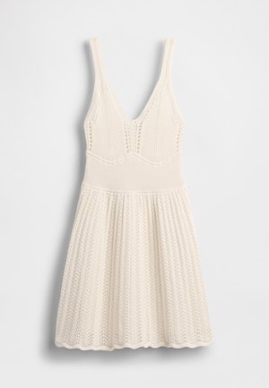 Stickad klänning i krämfärg med V-ringning, ribbad överdel och utsvängd kjol med vågig fåll och hålmönster över hela plagget.