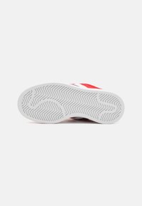 Zapatilla roja y blanca con una suela de goma blanca texturizada que presenta un patrón en zigzag y un diseño de perfil bajo adecuado para uso casual.