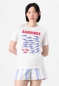 Balta trumpa rankovė t-shirt su mėlynu žuvies raštu ir raudonu užrašu "SARDINOS ITALIJA PRIE JŪROS". Audinys atrodo lygus ir pralaidus orui.