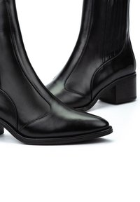 Botines de cuero negro con punta afilada, textura suave y tacón cuadrado. Paneles elásticos laterales para fácil uso y un diseño elegante.