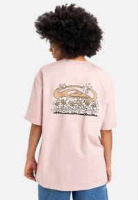 Rosa bomulds t-shirt med et grafisk print af smilende blomster og et svunget design i brun og sort på ryggen. Løs pasform, korte ærmer.