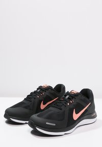 Black athletic shoes with a textured mesh upper, featuring a pink Nike swoosh and accents, white midsole, and black laces.