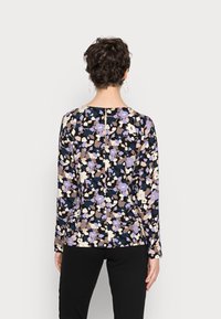 Blumenbluse mit langen Ärmeln. Schwarzer Hintergrund mit lila, beige und weißen Blumen. Der Rücken hat eine Schlüssellochöffnung mit Knopfdetails.