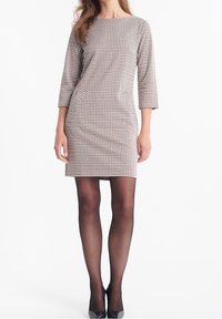 Brun och krämfärgad rutig klänning med trekvartslånga ärmar, figurnära passform och sidofickor, matchad med genomskinliga svarta strumpbyxor och klackar.