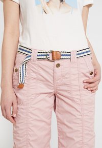 Różowe spodnie bojówki z bocznymi kieszeniami, wyposażone w paskowy pas z paskiem w paski, okrągłą metalową klamrą i skórzanym akcentem. Materiał ma delikatną fakturę.