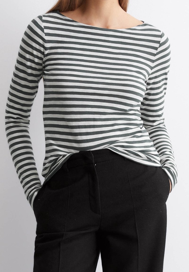 Langsleeve shirt met grijs-witte horizontale strepen, bootnek, zachte stof en een relaxte pasvorm, gecombineerd met zwarte broeken.