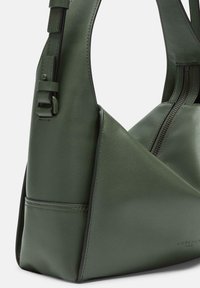 Zielona skórzana torebka na ramię o unikalnym, trójkątnym kształcie, z zamknięciem na zamek błyskawiczny i regulowanym paskiem.