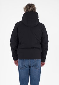 Zwarte hoodie-jack met een gevoerd ontwerp, een iets getailleerde silhoutte en een soepele textuur. Gecombineerd met blauwe jeans.