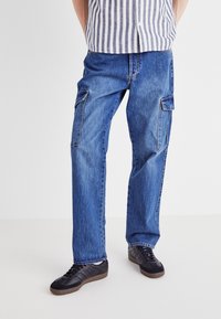 Blå denim cargo bukser med to sidelommer, lige ben design, synlig syning og en afslappet pasform, parret med sorte sportsko.