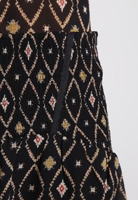 Jupe noire avec taille smockée, ornée d'un motif en losanges en filigrane doré, rouge et blanc. Texture de tissu léger.