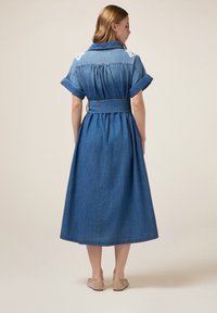 Denim shirtjurk met korte opgerolde mouwen, een ceintuur in de taille en een geplooide achterkant. Kleur: medium blauw. Beschikt over subtiele decoratieve stiksels.