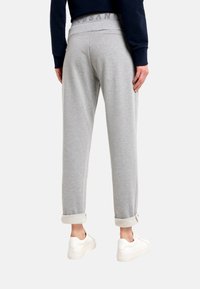 Grau melierte Jogginghose mit weicher Textur und umgeschlagenem Saum. Der elastische Bund ist dezent gebrandet. Kombiniert mit weißen Turnschuhen.