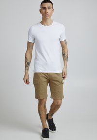 Vit kortärmad T-shirt i kombination med khaki cargoshorts med sidofickor. Bärs med svarta sneakers. Slät tyg och avslappnad passform.