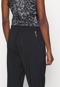 Svarta träningsbyxor i lätt material, med ett elastiskt midjeband och subtil logotypdetalj. Designen inkluderar en slät textur och enkel skärning.