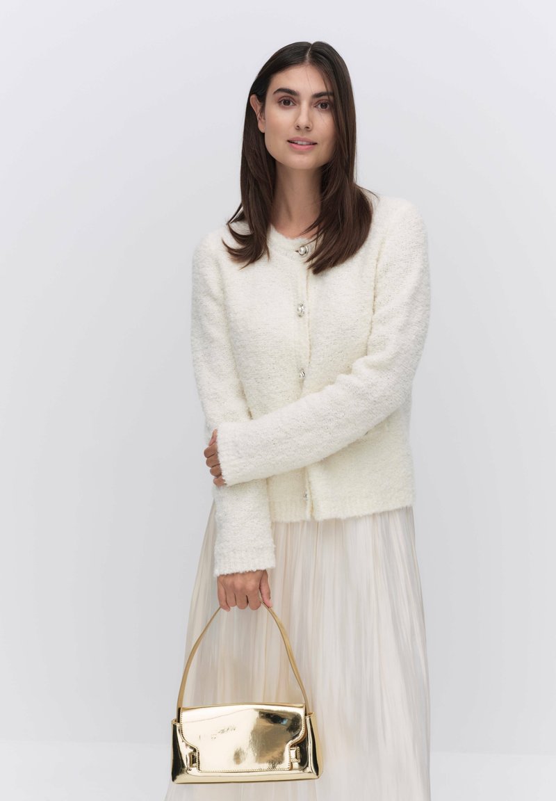 Witte, gemêleerde cardigan met lange mouwen en zilveren knopen; gecombineerd met een doorschijnende, geplooide rok en een kleine gouden handtas.