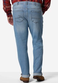 Jeans de denim azul claro con corte recto, que cuentan con dos bolsillos traseros, un desvanecimiento mínimo y un dobladillo enrollado. Llevados con zapatos marrones.