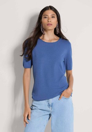 Blauw kortärmelig gebreide trui met een ronde hals, met een gladde textuur. Gecombineerd met lichtblauwe spijkerbroeken.