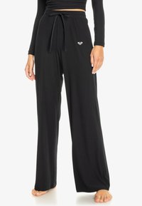 Black wide-leg pants made of ribbed fabric. Features a drawstring waist and a small heart logo on the left side. Smooth texture.