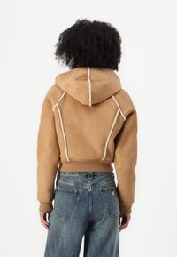 Sweat-shirt à capuche beige avec une texture douce, présentant des surpiqûres blanches contrastantes et des poignets côtelés. Assorti à un jean bleu taille haute.