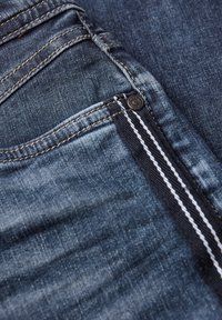 Jeans de denim de color azul profundo, con desvanecimientos claros, una cremallera estándar con herrajes negros y detalles de costura blanca.