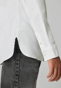 Witte lange mouwen shirt van een gestructureerde stof, met een ronde zoom en knoopmanchetten, gecombineerd met donkergrijze denim. Subtiele details op de mouwen.