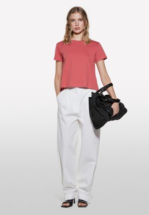 Red cropped t-shirt, white high-waisted trousers, and black oversized handbag. Black heeled sandals complete the look.