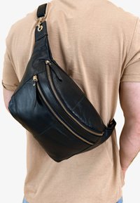 Bolso bandolera de cuero negro con múltiples bolsillos con cremallera, acentos de hardware dorado y una textura suave. El diseño tiene una forma ergonómica para mayor comodidad.