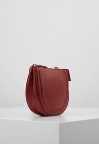 Czerwona skórzana torebka na ramię o zaokrąglonym kształcie, teksturowanej powierzchni i subtelnych akcentach szwów. Posiada zamek błyskawiczny oraz kompaktowy kształt.